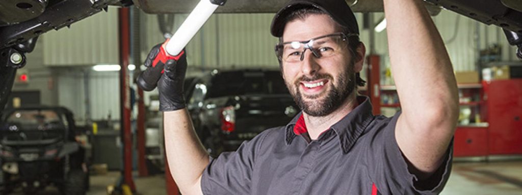 auto service technology adult student examines the underside of a car with a light