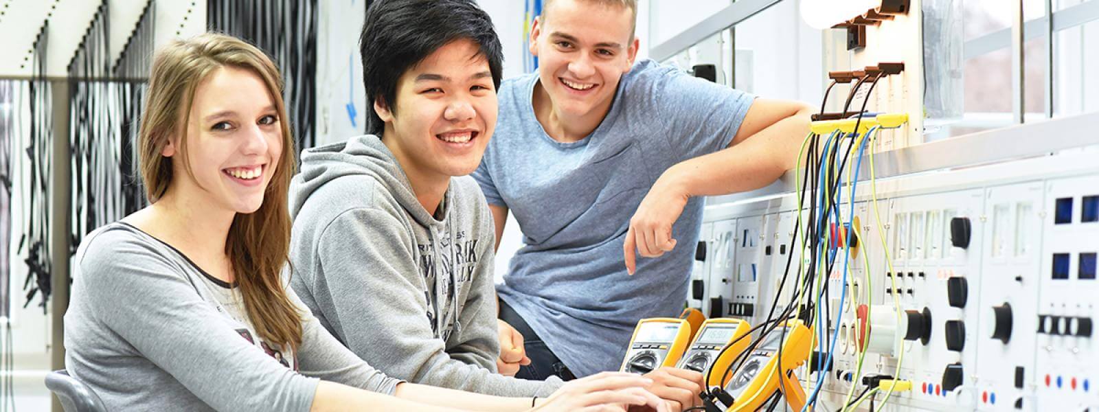 Three pre engineering students smile for a photo by a computerized panel