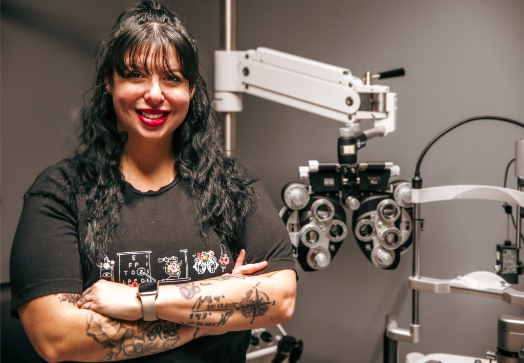 CV Tech student Brandi Swindler stands with arms folded in front of a phoropter inside the Vision Care Technician classroom at the school's Cowan Campus near Yukon.
