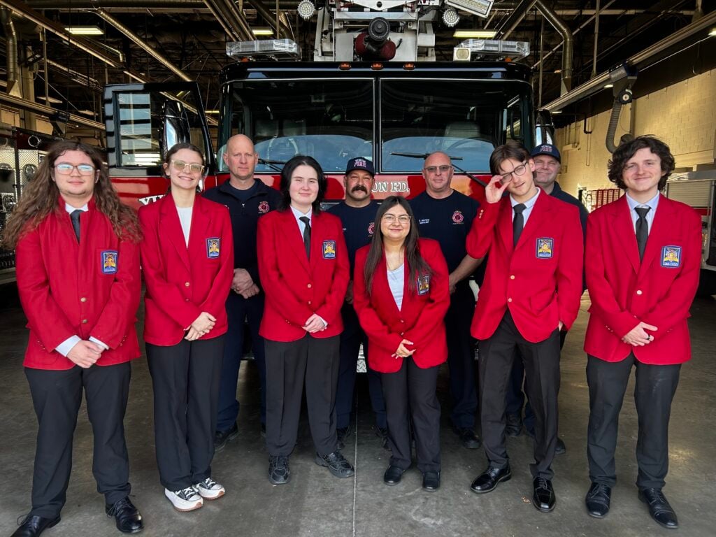 Six CV Tech students, dressed in bright, red blazers, stand in front of three Yukon Fire Department personnel and a fire engine.