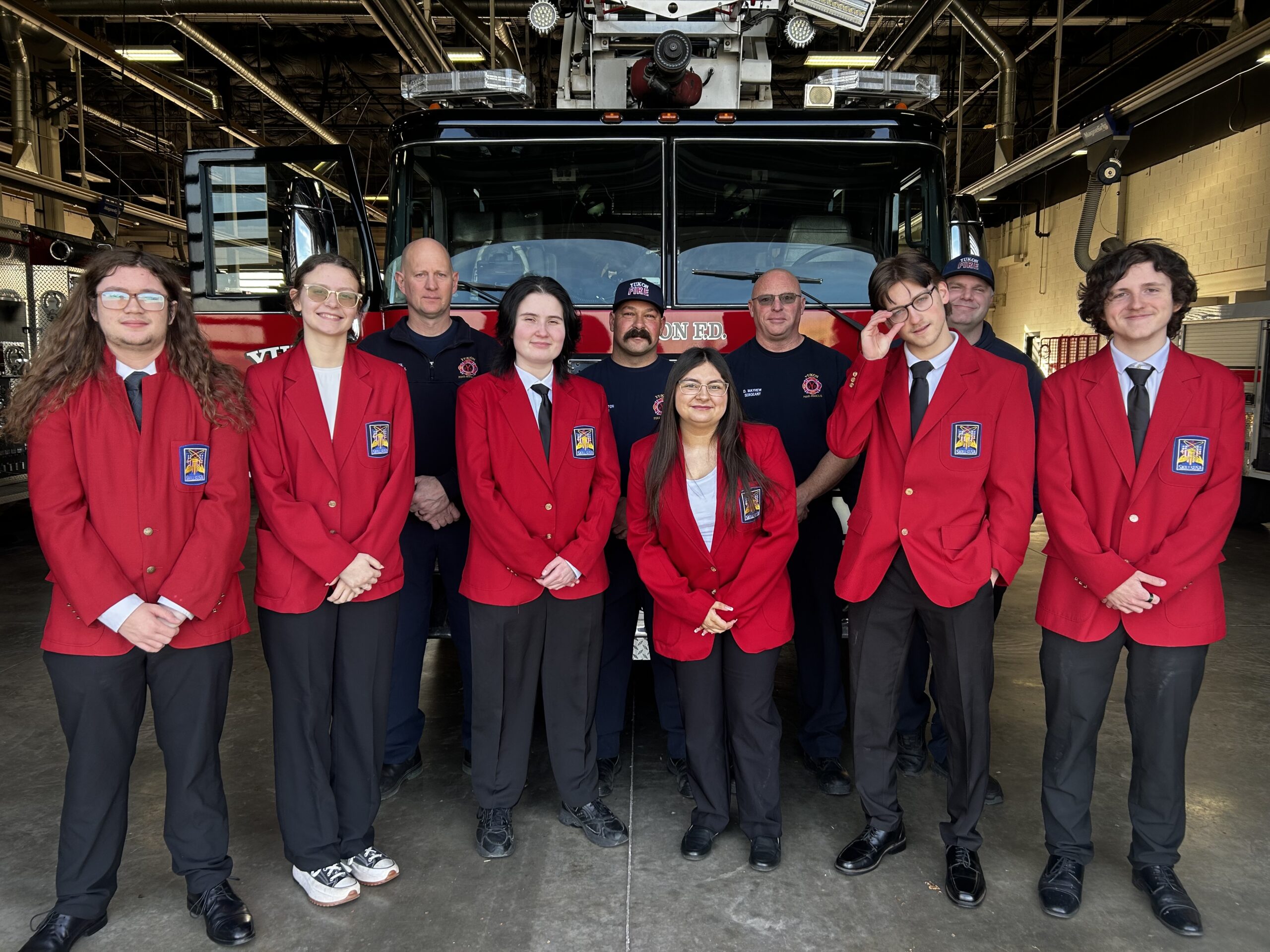 Six CV Tech students, dressed in bright, red blazers, stand in front of three Yukon Fire Department personnel and a fire engine.