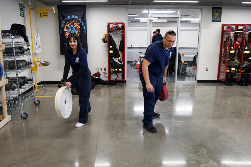 A female and male student enrolled in CV Tech's Firefighter program prepare to unroll hoses on a concrete floor.