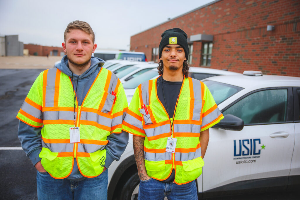 Quincy Jones, El Reno, and Jacob Adams wearing bright yellow safety vests stand in front of a fleet of small, white USIC SUVs.