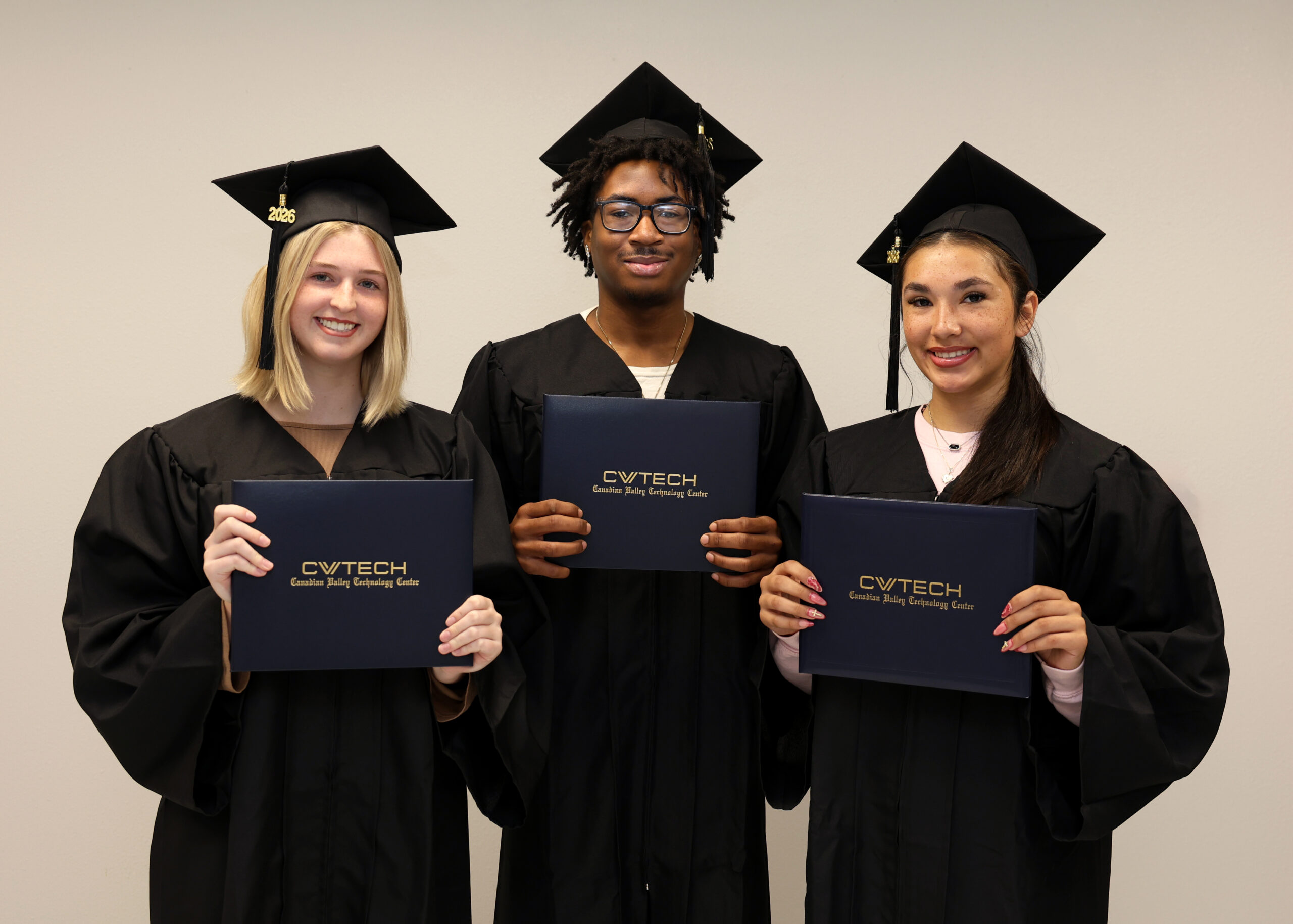 three students stand in caps and gowns holding CV Tech diploma covers.