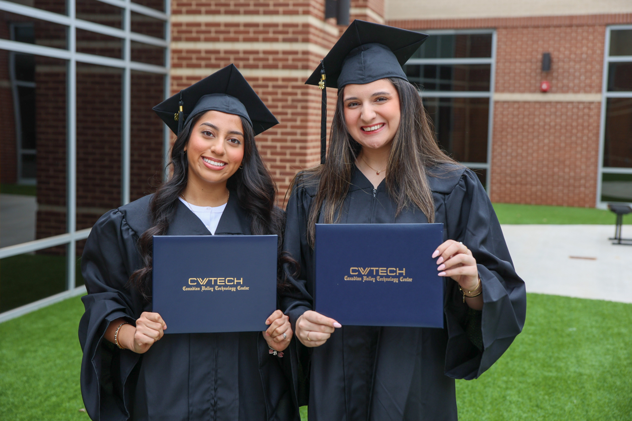 Two students in caps and gowns hold CV Tech diploma covers in Cowan's courtyard.