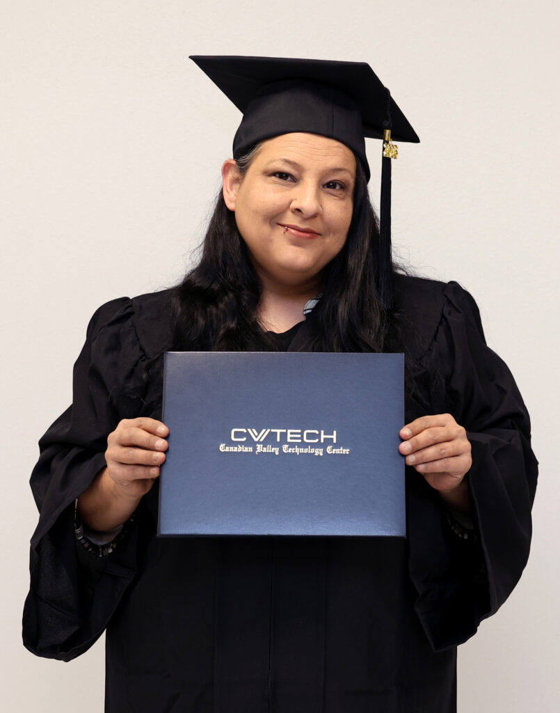 A woman dressed in graduation regalia holds a CV Tech diploma cover.