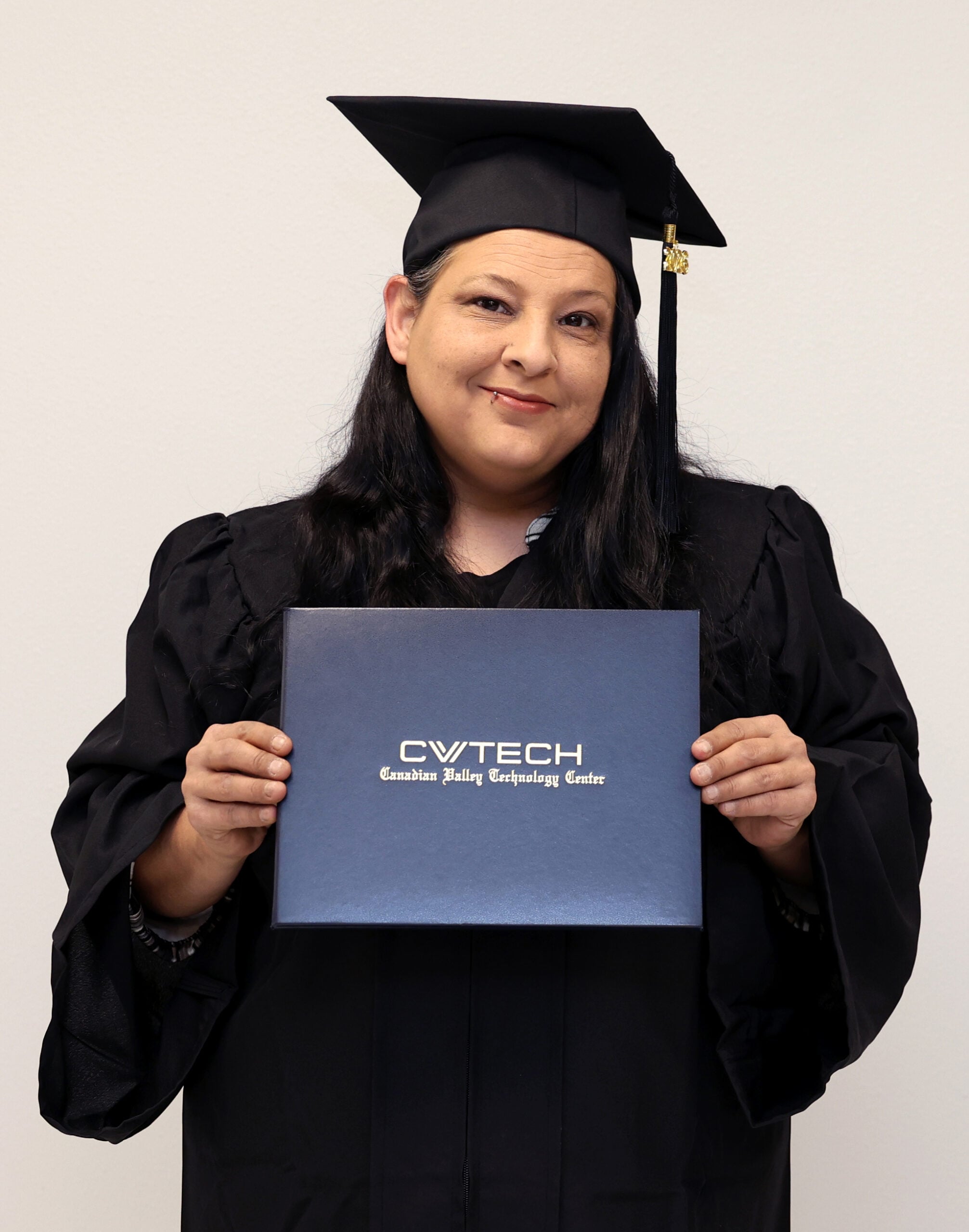 A woman dressed in graduation regalia holds a CV Tech diploma cover.