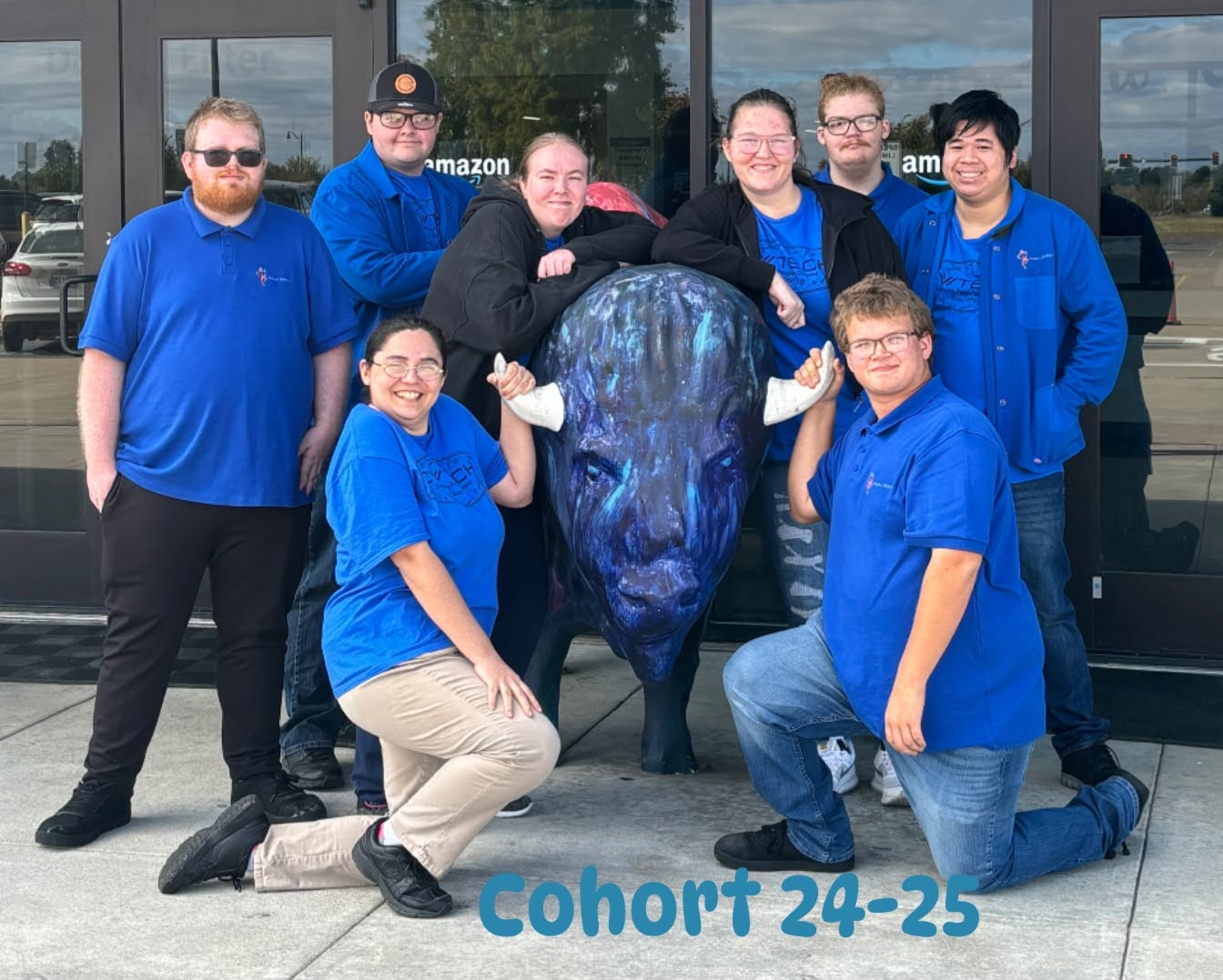Eight students in blue shirts stand beside a blue buffalo statue.