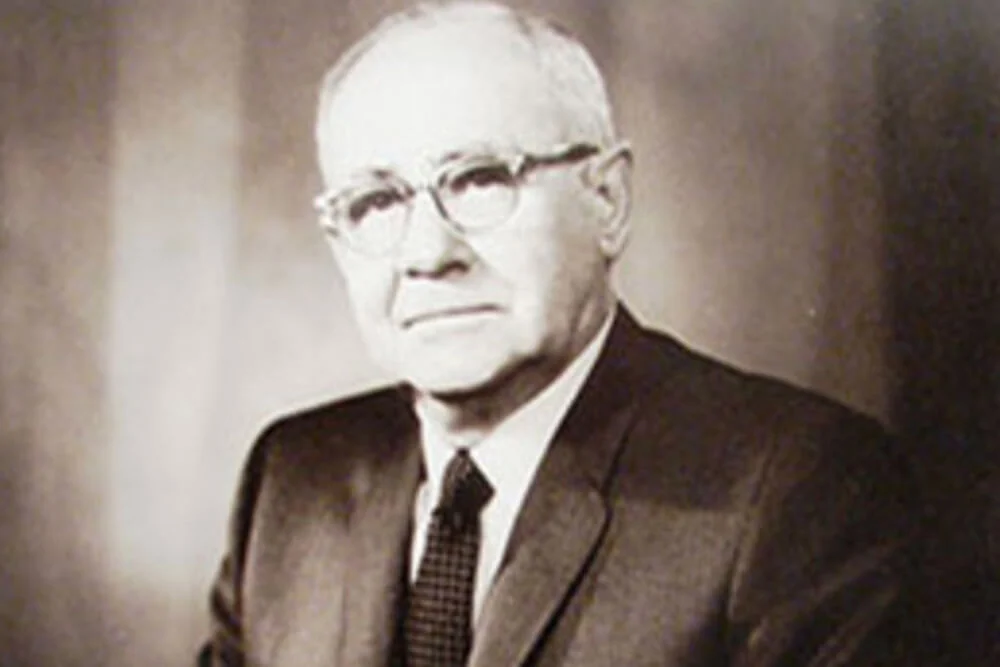 This is a black and white photo of an older gentleman wearing a suit and eyeglasses.